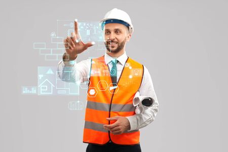 Front view of smiling architect with paper rolls wearing reflective vest and helmet. Digital tactile...