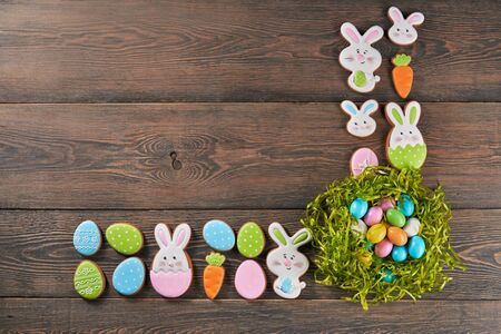 From above view of colorful ginger glazed cookies and eggs in green nest isolated on wooden...
