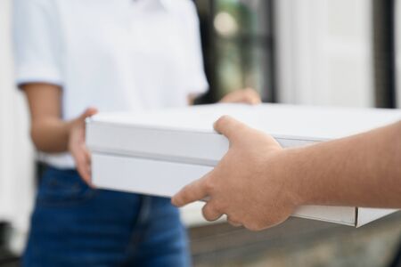 Selective focus of male hands giving two boxes of pizza to woman. Close up of incognito female in casual outfit receiving order from deliveryman outdoors. Food delivery concept.の写真素材