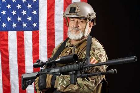 Front view of old military officer holding sniper rifle and looking at camera. Portrait of bearded...