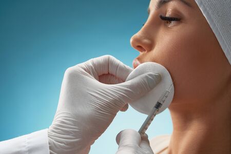 Close up of cosmetic injection in female cheek. Cosmetologist using syringe with special liquid and...