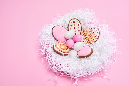 From above view of glazed cookies in shape of lovely eggs with pattern and colorful real eggs lying in white nest isolated on pink background. Close up of cute pastry. Easter holidays concept.の写真素材