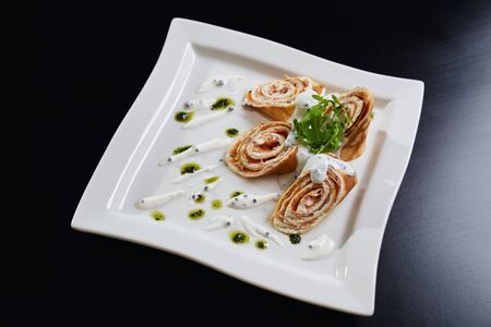 Top view of four sliced rolls with paste and salmon served with salad rocket, pesto and sour cream on white plate. Tasty dish isolated on black wooden table in restaurant. Concept of cuisine.の写真素材