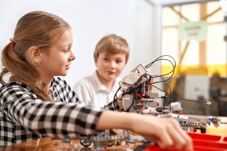 Side view of boy helping girl in creating robot using building kit for kids on table. Science engineering. Nice interested friends smiling, chatting and working on project together.の写真素材