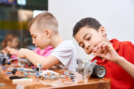 Side view of building kit with colorful pieces in box for group of multiracial kids creating robots, having positive emotions and joy. Close up of interested friends working on project.の写真素材