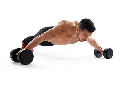 Muscular shirtless caucasian bidybuilder training on floor using dumbbells, isolated on white studio background. Close up of young sportsman building muscles, doing wide push ups. Concept of sport.の写真素材