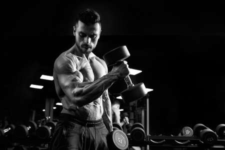 Side view of shirtless male bodybuilder training biceps with dumbbell. Close up of sportsman with...