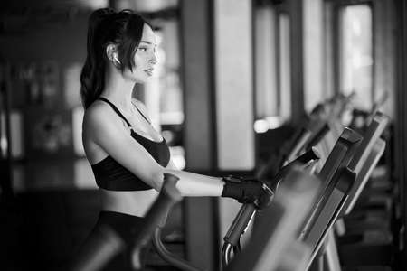 Side monochrome view of brunette woman in sport top and gloves doing hard cardio workout on...