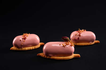 Pink cakes decorated with nuts and dry rose flower isolated on black background. Dessert with smooth...