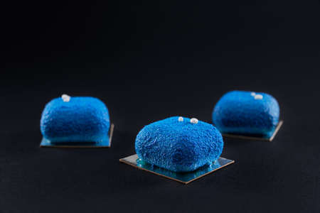 Closeup view of matte blue dessert decorated with white balls isolated on black studio background. Three small matte cakes in row in restaurant. Concept of confectionary.の写真素材