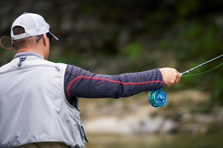 Back view of professional fisherman in special uniform using spinning for fishing in mountain river....