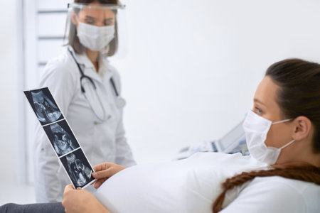 Professional gynecologist showing to pregnant woman ultrasound scan of her baby. Maternity during...