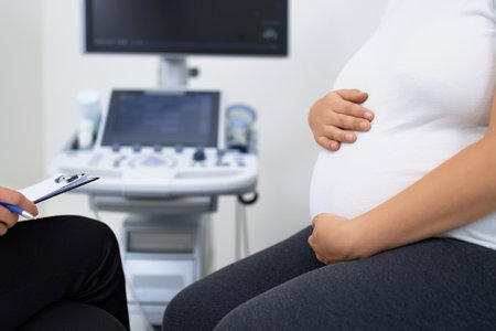 Close up of pregnant woman in white t-shirt holding hands on her tummy during medical checkup at...