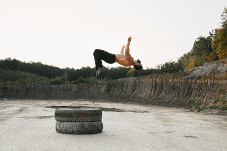 Muscular man with bare torso jumping high during outdoors workout of fresh air. Strong guy in pants...