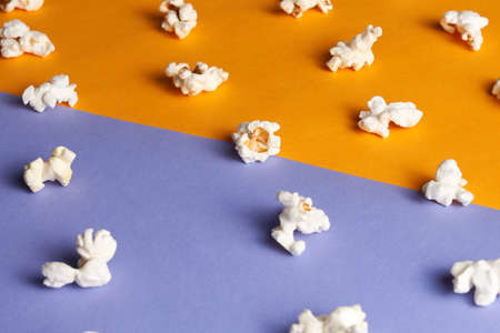 Diffrent pieces tasty popcorn on half orange half violet background. Concept of movie.の写真素材