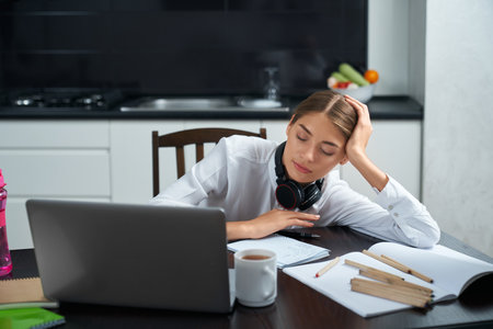 Sleepy young woman in white shirt sitting at table with opened laptop and taking nap. Exhausted...