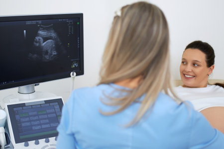 Back view of female gynecologist doing ultrasound diagnostic of pregnant woman and looking at...