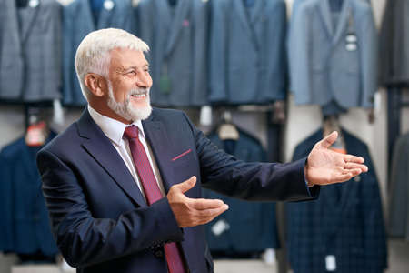 Happy senior man with grey hair smiling and choosing new collection costumes in store. Concept of shopping.の写真素材