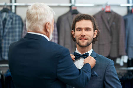 Close up of senior man helping son choose bow tie in store. Concept of purchase in boutique for men.の写真素材