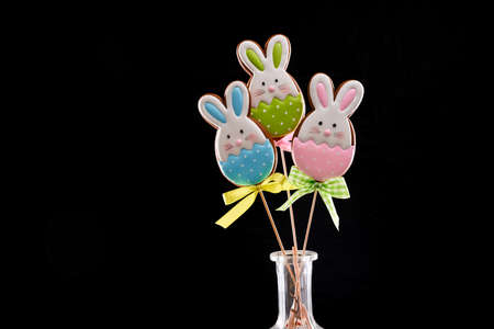 Easter gingerbread bunnies with colorful icing on wooden stick with bows. Isolated over black...