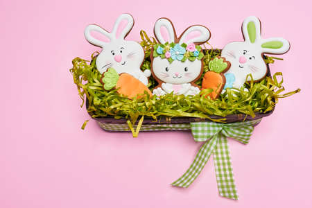 Easter basket with cute decor made of homemade bunny and carrot cookies over pink background....