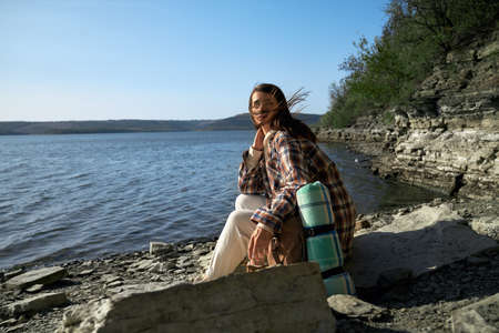 Peaceful young woman with brown hair sitting at riverside and enjoying amazing nature at Bakota bay. Dniester river on background. Concept fo travelling.の写真素材