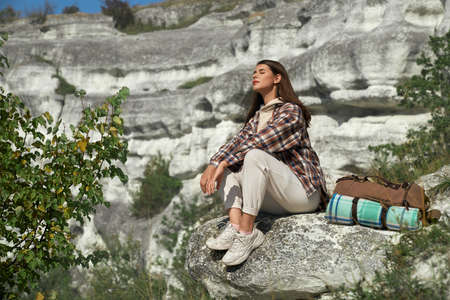 Young woman with brown hair relaxing on rock, keeping her eyes closed and enjoying favorite hobby outdoors. Pretty lady spending active leisure time at national ukrainian park.の写真素材