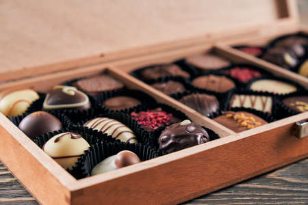 Close up of wooden box with delicious sweets made of milk, white and black chocolate. Variety of...