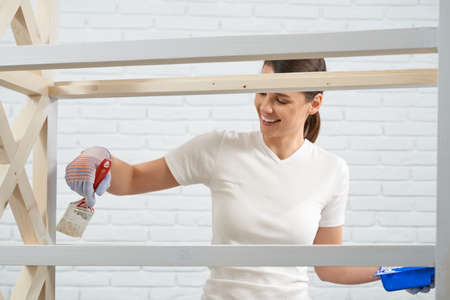 Close up of young brunette smiling and painting in white color rack at home. Concept of process...