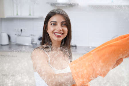 Close up of smiling cute woman washing glass with rag in kitchen. Concept of house cleaning.の写真素材