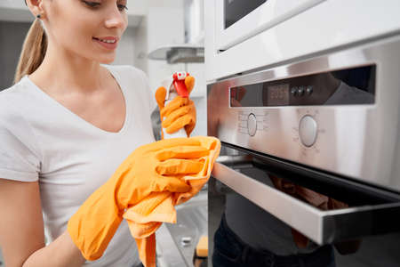 Close up of young woman cleaning oven with special detergent in kitchen. Concept of process chores.の写真素材