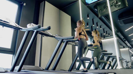 Side view of young woman with good body in sportswear running on treadmill near mirror in modern gym. Concept of healthy lifestyle for pump up body.の写真素材