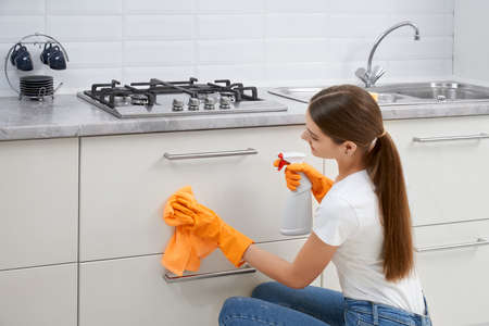 Close up of young woman cleaning kitchen furniture in rubber gloves. Concept of house cleaning.