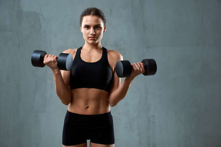 Front view of muscular caucasian woman training with dumbbells and looking at camera. Isolated...