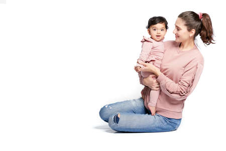 Portrait of mother with smiling baby daughter isolated on white studio background. Side view of...