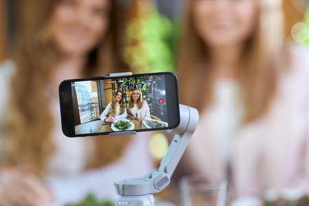 Close up of two beautiful young blogger women posing on phone camera. Concept of process photo shoot...