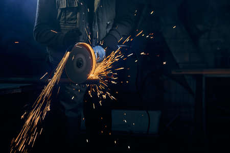 Close up of fitter in special suit cutting with rotating disc for metal with large sparks. Concept...
