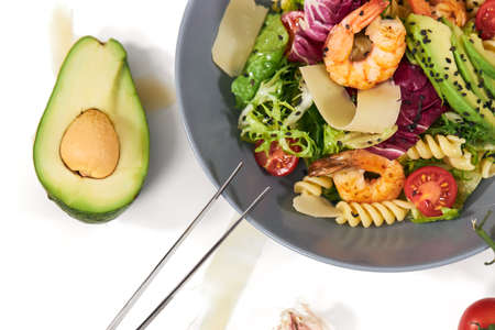 Top view close up of healthy and appetizing pasta with shrimps,tomatoes,avocado and herbs on white background. Concept of delicious dish with healthy ingredients for body weight maintenance.の写真素材