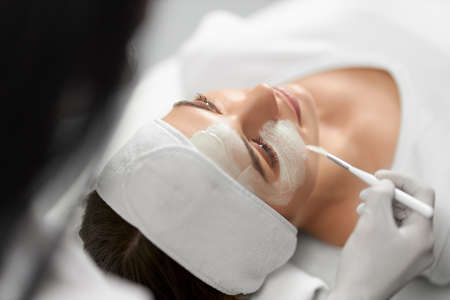 Side view of beautician in white rubber gloves doing peeling face for young attractive patient....