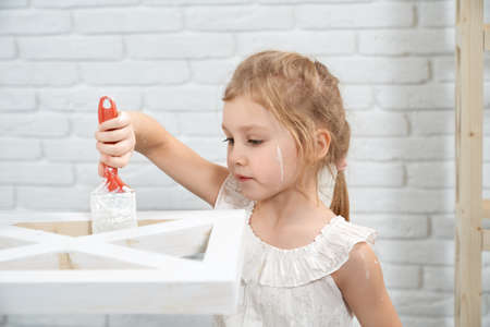 Close up of smiling cute little girl holding bush and painting rack in white color. Concept of repair at home.の写真素材