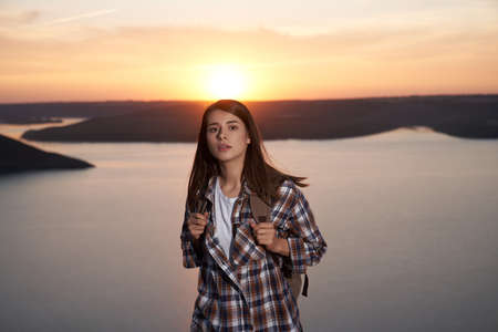 Adorable female tourist with backpack posing during amazing sunset at Bakota bay. Happy woman with brown hair walking outdoors during evening time.の写真素材