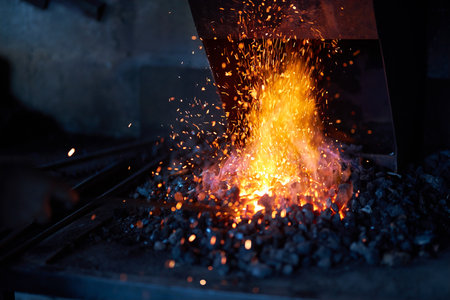 Red hot metal in burning fire preparing for forging process at workshop. Sparks flying around. Traditional blacksmith manufacture.の写真素材