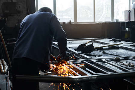 Craftsman in uniform using angle grinder for polishing metal at workshop garage. Competent worker...