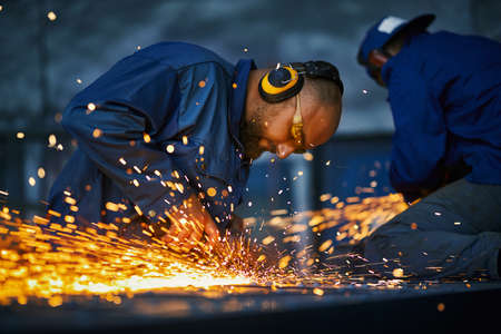 Group of two craftsmen in protective uniform welding metal construction. Spark from metalworking. Concept of people, industry and manufacture.