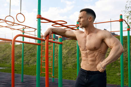 Shirtless caucasian man with muscular torso standing on sports ground outdoors. Active bodybuilder...