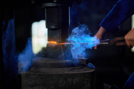 Caucasian craftsman in uniform putting heated metal under press machine at workshop. Close up of...