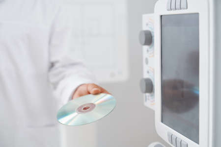 Crop of male doctor holding plate with silver CD plate with information and results after ultrasound...