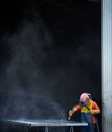Male operator of sandblasting machine wearing protective uniform while polishing metal at workshop. Man preparing details for painting.の写真素材