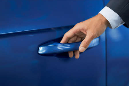 Close up of male hand holding handle of luxury blue car. Man in suit opening door of his new modern vehicle. Concept of people and transport.の写真素材