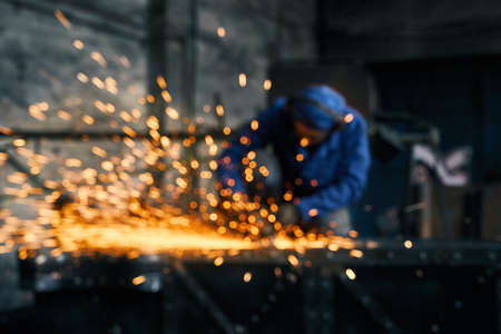 Close up of young man in blue special uniform doing gate by electric steel cutter machine for welding special metal. Concept of process produce modern fence in garage.の写真素材